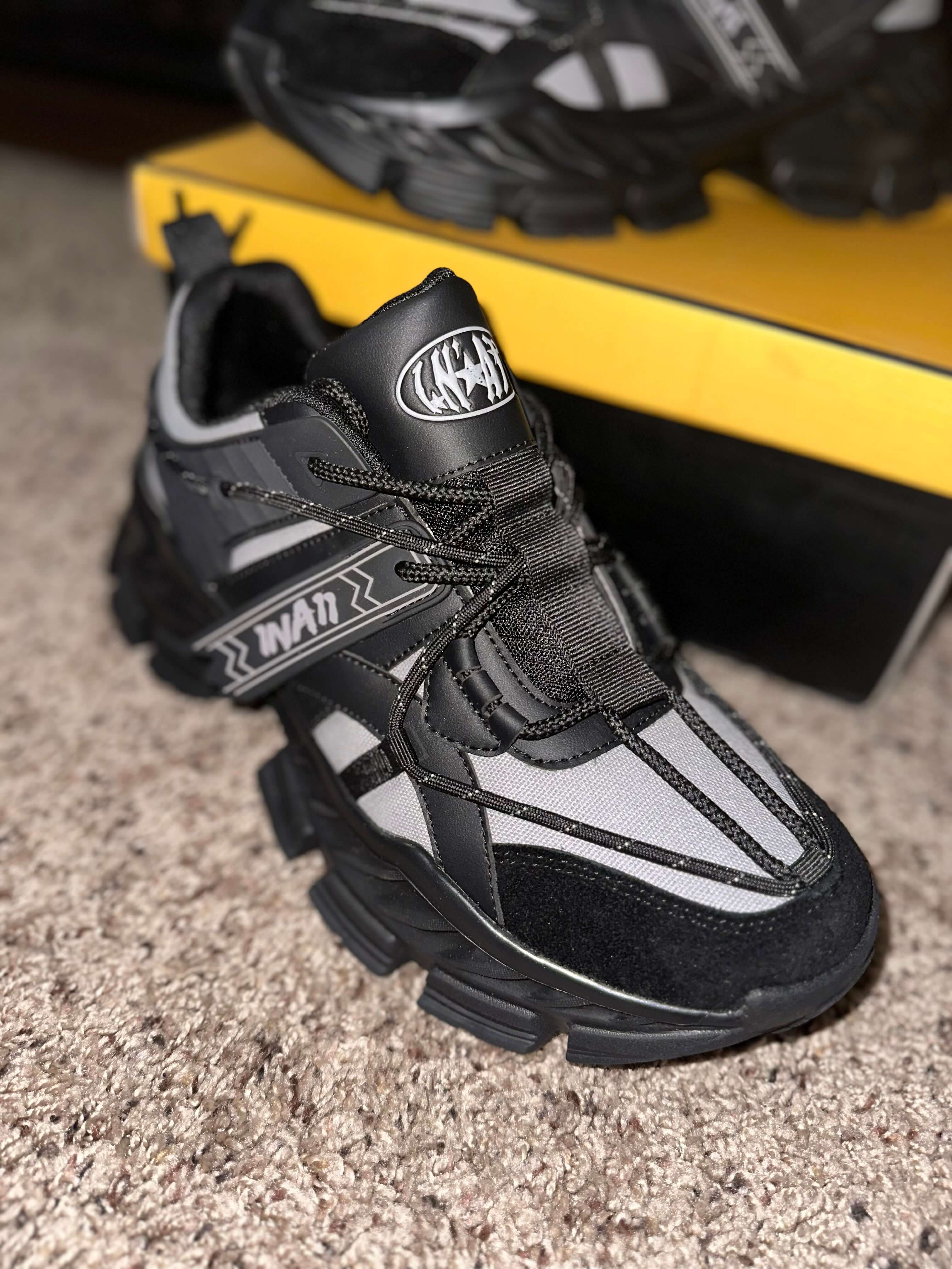 1 N' A11 Charcoal Glaze black and grey sneakers on carpet with yellow box in the background.