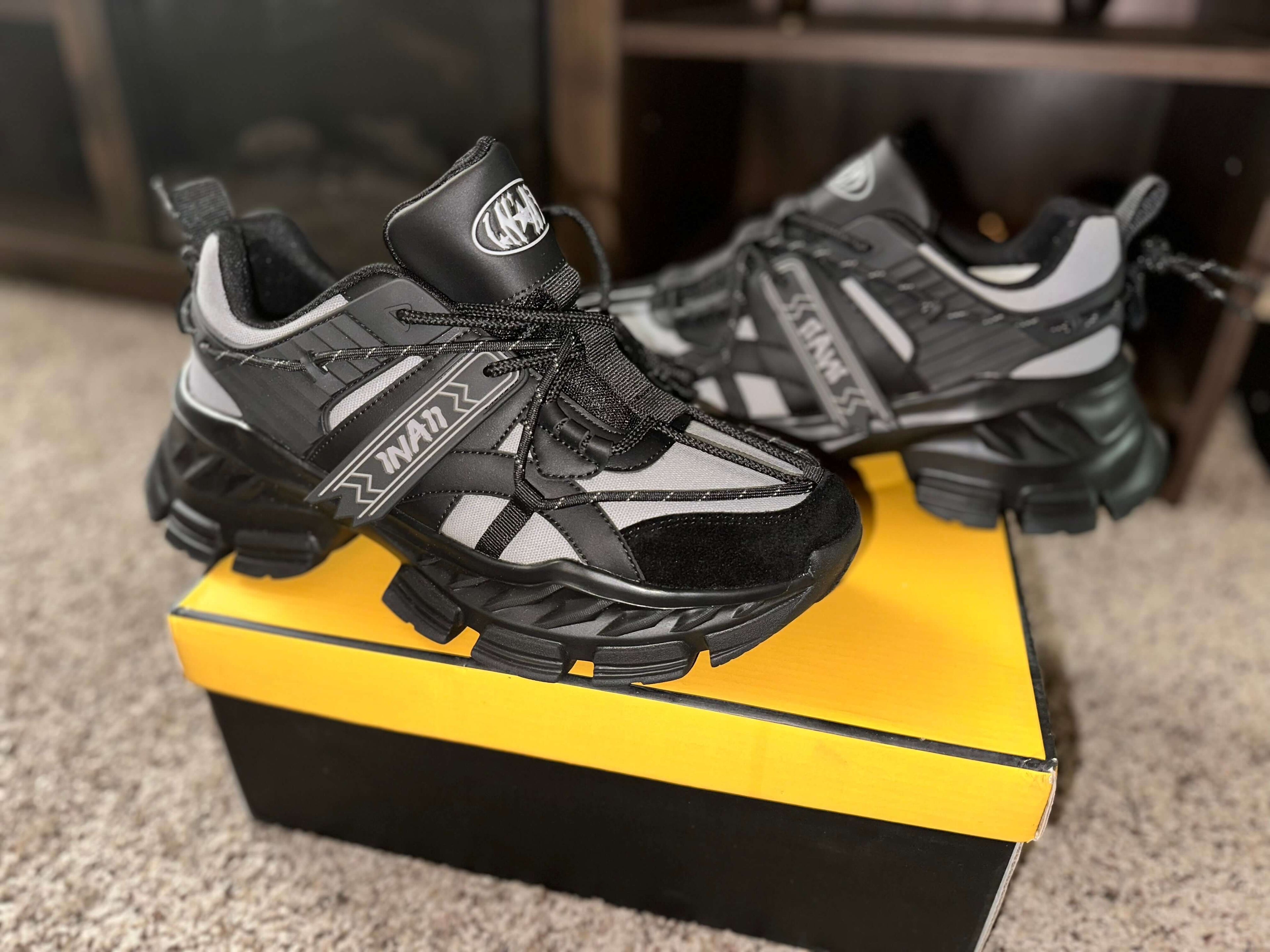 1 N’ A11 Charcoal Glaze Sneakers in black and grey on a yellow shoebox, showcasing their stylish design and robust build