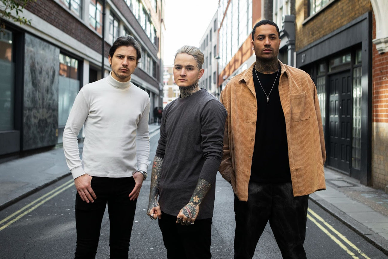 Three young men showcasing premium streetwear on an urban street. Their stylish outfits, including a white turtleneck, grey shirt with tattoos, and tan corduroy jacket, reflect modern street fashion.