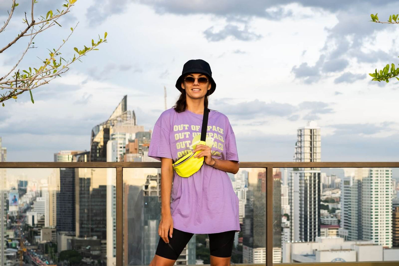 Stylish woman in an oversized purple t-shirt with neon waist bag on the rooftop with city skyline background