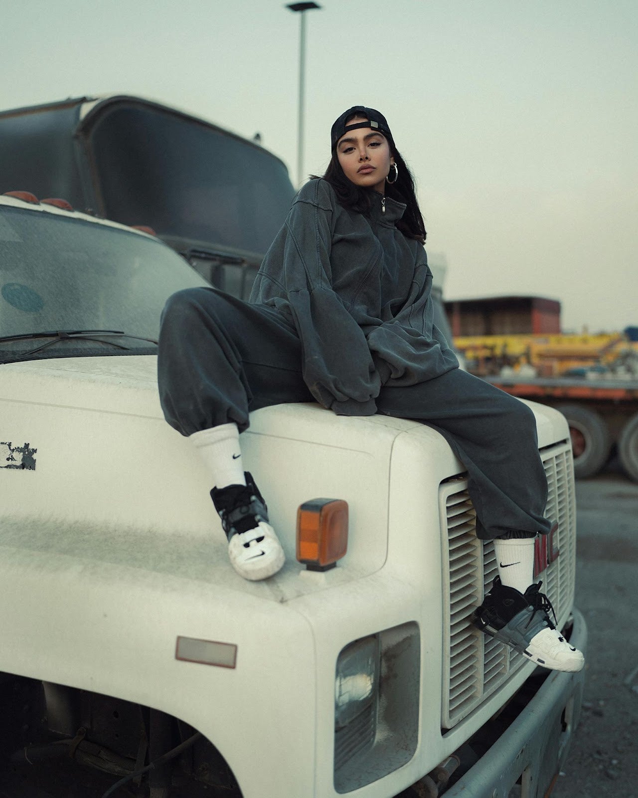A woman styling oversized streetwear, including a baggy sweatshirt, cap, and sneakers, showcasing the relaxed and trendy look.
