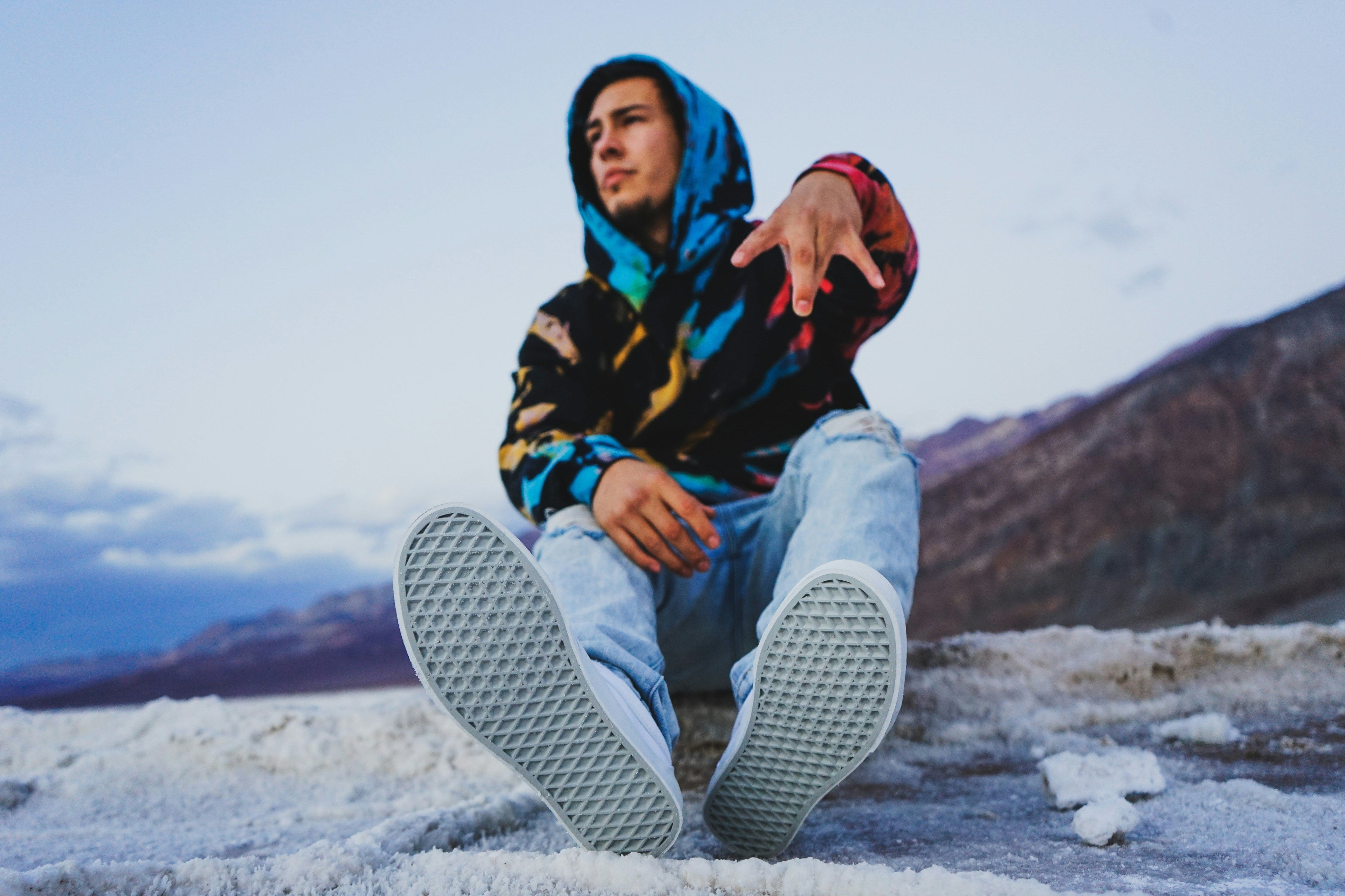 A stylish man wearing a colorful hoodie, ripped jeans, and sneakers poses outdoors, showcasing modern streetwear fashion with a bold urban vibe.